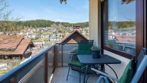 A balcony with a view of a town, a table with a chair, and a potted plant.