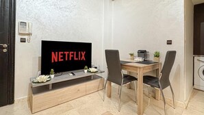A modern living room with a flat-screen TV displaying 'NETFLIX', a wooden dining table with two chairs, a small plant, and a coffee machine. - Bewitchment in Marrakech: A haven of peace in Guéliz, close to Carré Éden (Marrakech)