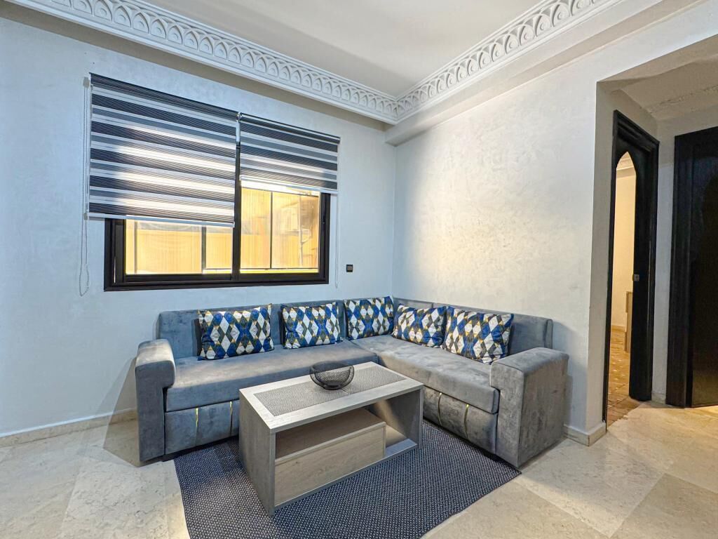A modern living room with a grey sectional sofa, a coffee table, and a large window with blinds.