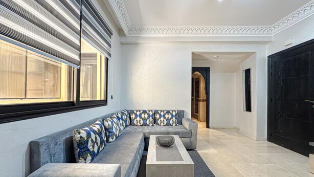 A modern living room with a grey sectional sofa, a coffee table, and a large window with blinds. - Bewitchment in Marrakech: A haven of peace in Guéliz, close to Carré Éden (Marrakech)
