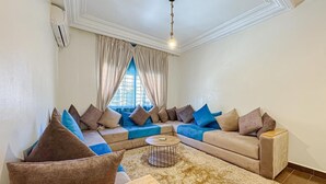 A living room with a sectional sofa, a round coffee table, and a large window with curtains.