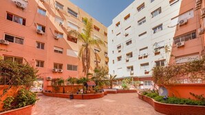 A courtyard with a brick pathway, surrounded by multi-story buildings with balconies and air conditioning units.
