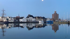 Ruhiges Ufer mit traditioneller Bebauung, einem hohen Gebäude und blauem Himmel.