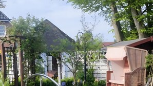 Ein Gartenweg führt zu einem Gebäude mit geneigtem Dach, umgeben von üppiger Vegetation und verschiedenen Pflanzen.