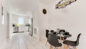 A modern kitchen with white cabinets, a stainless steel refrigerator, and a dining area with black chairs and a table set for four.
