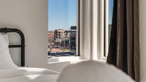 A hotel room with a bed, a window with curtains, and a view of buildings outside.