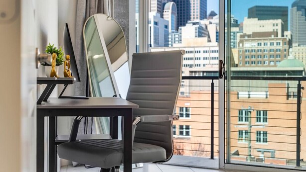 A modern office chair and desk by a large window with a city view.