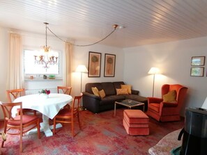 Ein Wohnzimmer mit Esstisch, Stühlen, einer Couch, einem Couchtisch und einem roten Sessel.