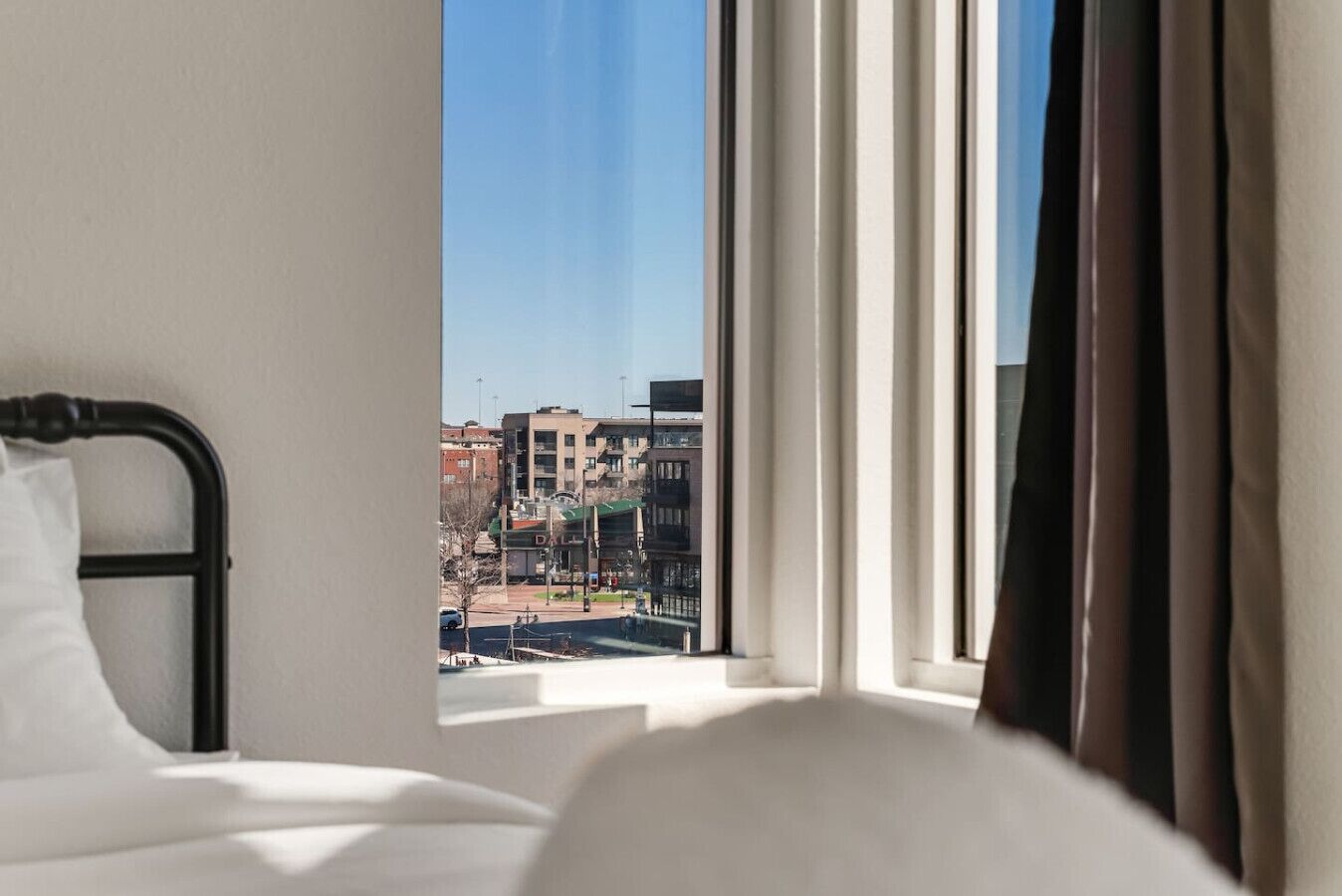 A hotel room with a bed, a window with curtains, and a view of buildings outside.