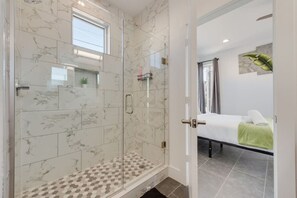 Un baño moderno con cabina de ducha de vidrio, cama con toalla verde y ventana que proporciona luz natural.