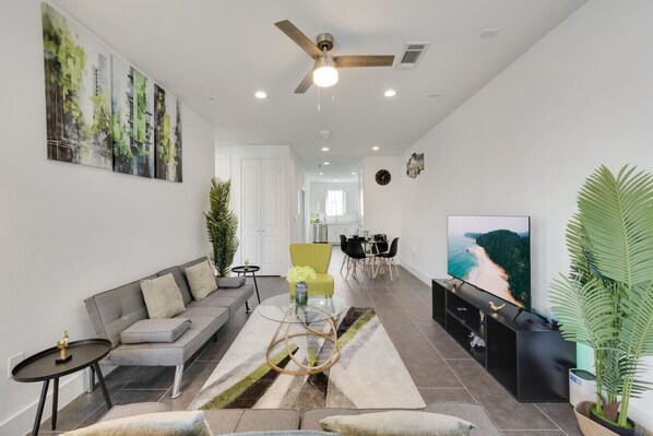 Una sala de estar moderna con un sofá gris, un sillón amarillo, una mesa de centro de vidrio y un televisor de pantalla plana.