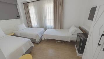A hotel room with two single beds, a small table, a yellow chair, and a kitchenette.