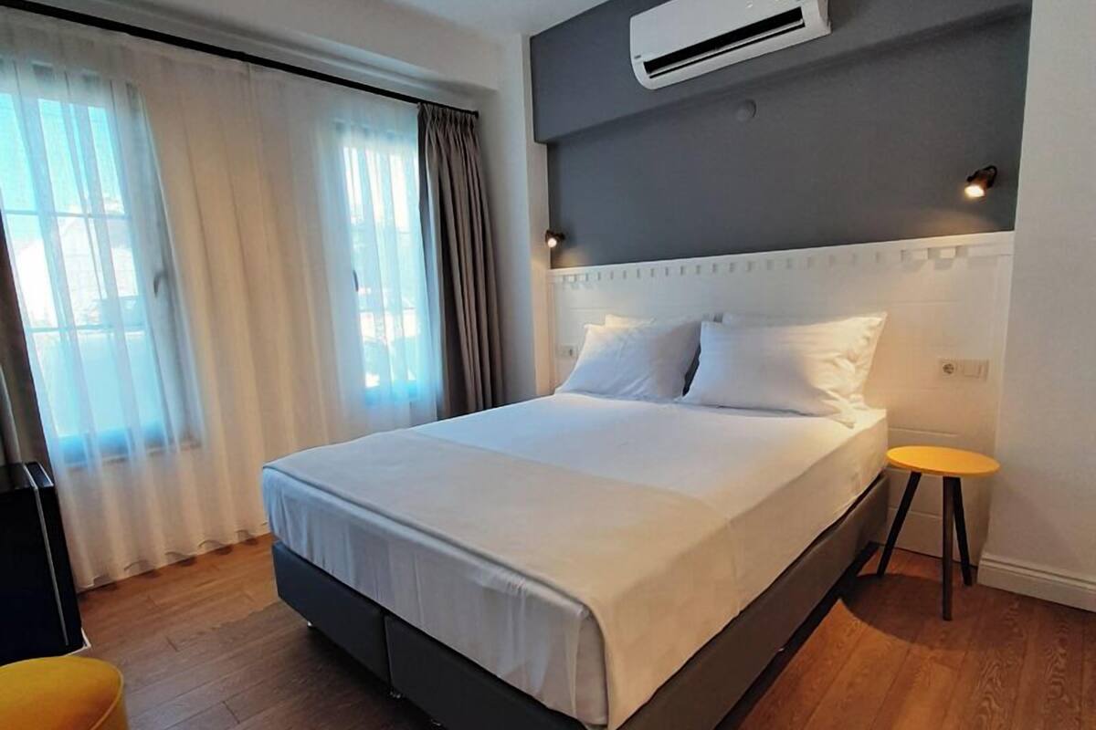 A modern hotel room with a large bed, a small table, and an air conditioning unit on the wall.