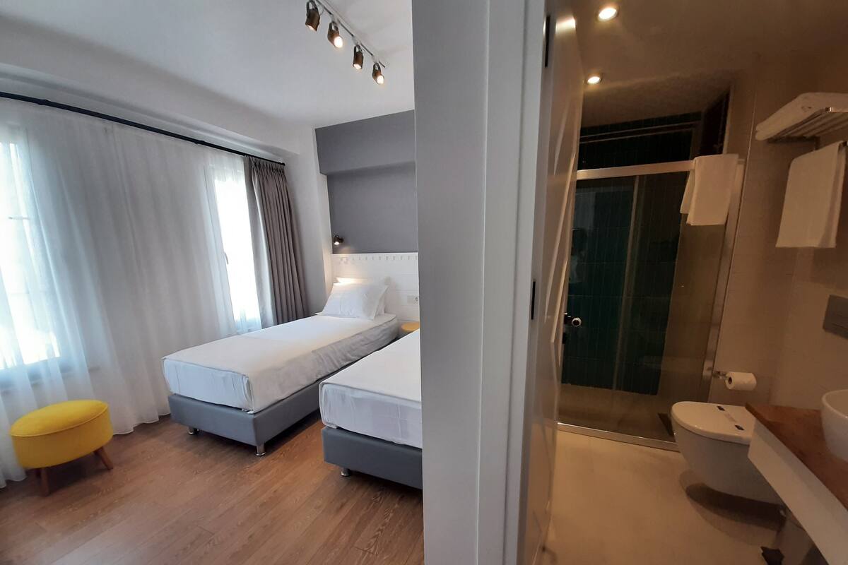 A hotel room with two single beds, a yellow chair, a shower, and a toilet.