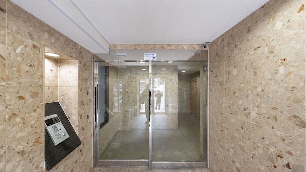 Een hal met een glazen deur die leidt naar een kamer. De wanden zijn betegeld met een puntpatroon.