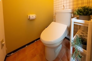 Ett badrum med en toalett, en toalettpappersrulle, en krukväxt och ett kaklat golv.