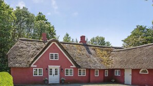 A red building with a thatched roof, white doors, and windows, surrounded by a gravel driveway and greenery.