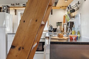 A modern kitchen with a wooden chair, a cutting board with a loaf of bread, a coffee maker, and a sink. - Cozy holiday apartment on Rømø (Rømø)