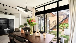 Una cucina moderna con mobili scuri, un tavolo da pranzo con sedie e un'ampia finestra che si affaccia su una scala e un giardino esterno.