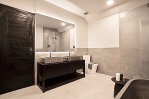 A modern bathroom with a dark wooden door, a large mirror, a black vanity, and a bathtub.