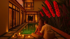 Una coppia seduta accanto a una piscina, con candele, un'ampia finestra e un'elaborata composizione floreale rossa.