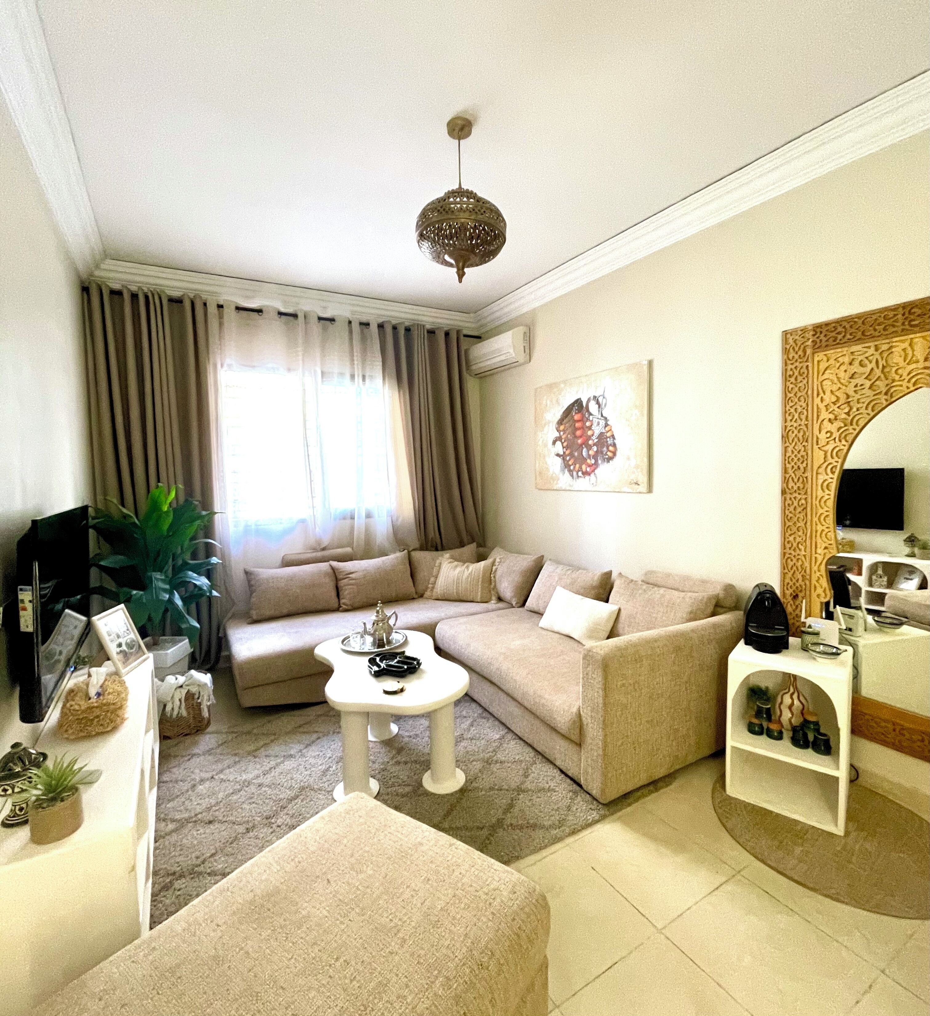 A living room with a beige sofa, a coffee table, a TV, a plant, and a decorative mirror.