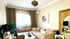 Un salon avec un canapé beige, une table basse, un téléviseur, une plante et un miroir décoratif.