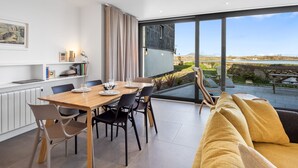 A modern living room with a large window, a dining area with a table set for four, and a cozy sofa.
