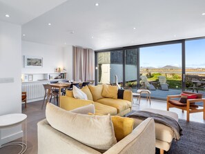 A modern living room with a large sofa, a dining area, and a view of the outdoors.