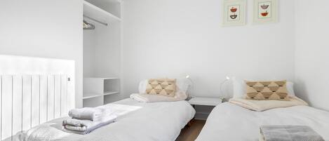 Een moderne, minimalistisch ingerichte slaapkamer met twee bedden, wit beddengoed en een witte radiator.
