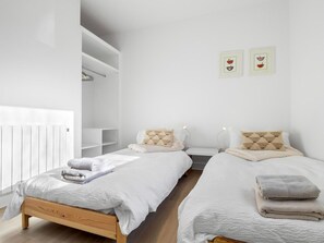 Un dormitori modern i minimalista amb dos llits, roba de llit blanca i un radiador blanc.