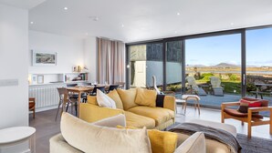 A modern living room with a large sofa, dining area, and a view of the outdoors.