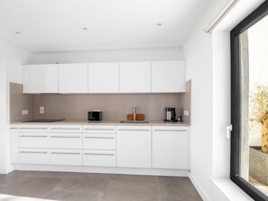 A modern kitchen with white cabinetry, a countertop, and a window with a view of a tree.