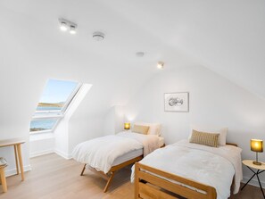A bedroom with two beds, a skylight, a bedside table, a lamp, and a framed picture on the wall.