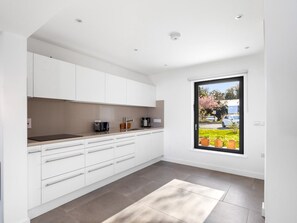 A modern kitchen with white cabinetry, a countertop, and a window with a view of a garden and parked cars.