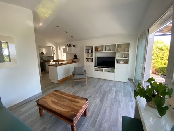 A modern living room with a wooden coffee table, a grey sofa, and a TV on a white entertainment unit. - Mini-villa with ocean view, sleeps 4, air conditioning and Wi-Fi, near the beach and shops! (Lumio)