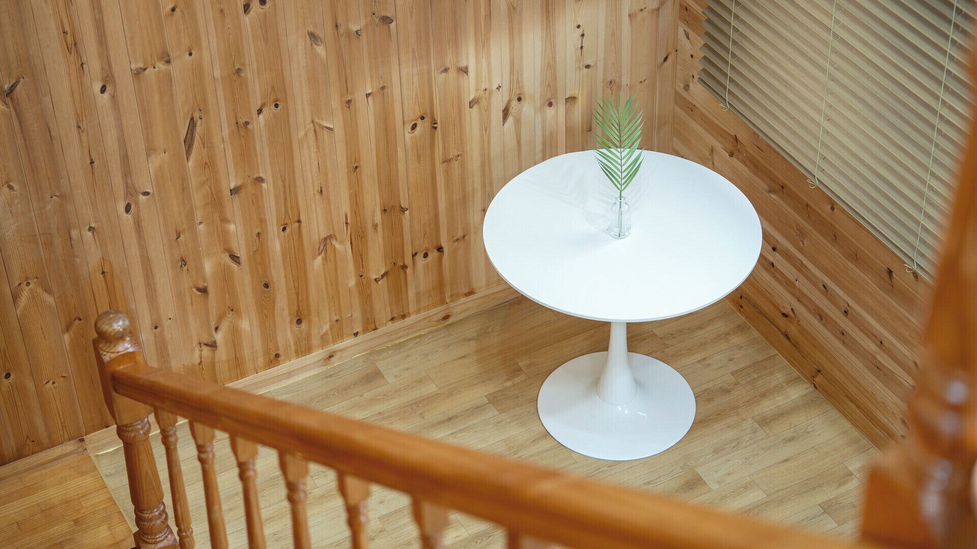 Una escalera con barandilla de madera y un pequeño descansillo con una mesa blanca, un florero de cristal y una planta verde.