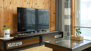 A modern living room with a large flat-screen TV mounted on a wooden wall, a glass coffee table, and a flower pot on the side.