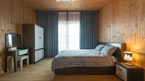 A bedroom with a bed, bedside table, lamp, dresser, and a desk with a mirror and plant.
