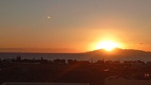 Een zonsondergang boven een kustlandschap met een berg op de achtergrond.