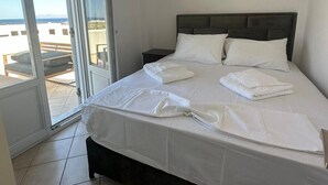 Een slaapkamer met een bed, nachtkastje en uitzicht door een glazen deur op een buitengebied.