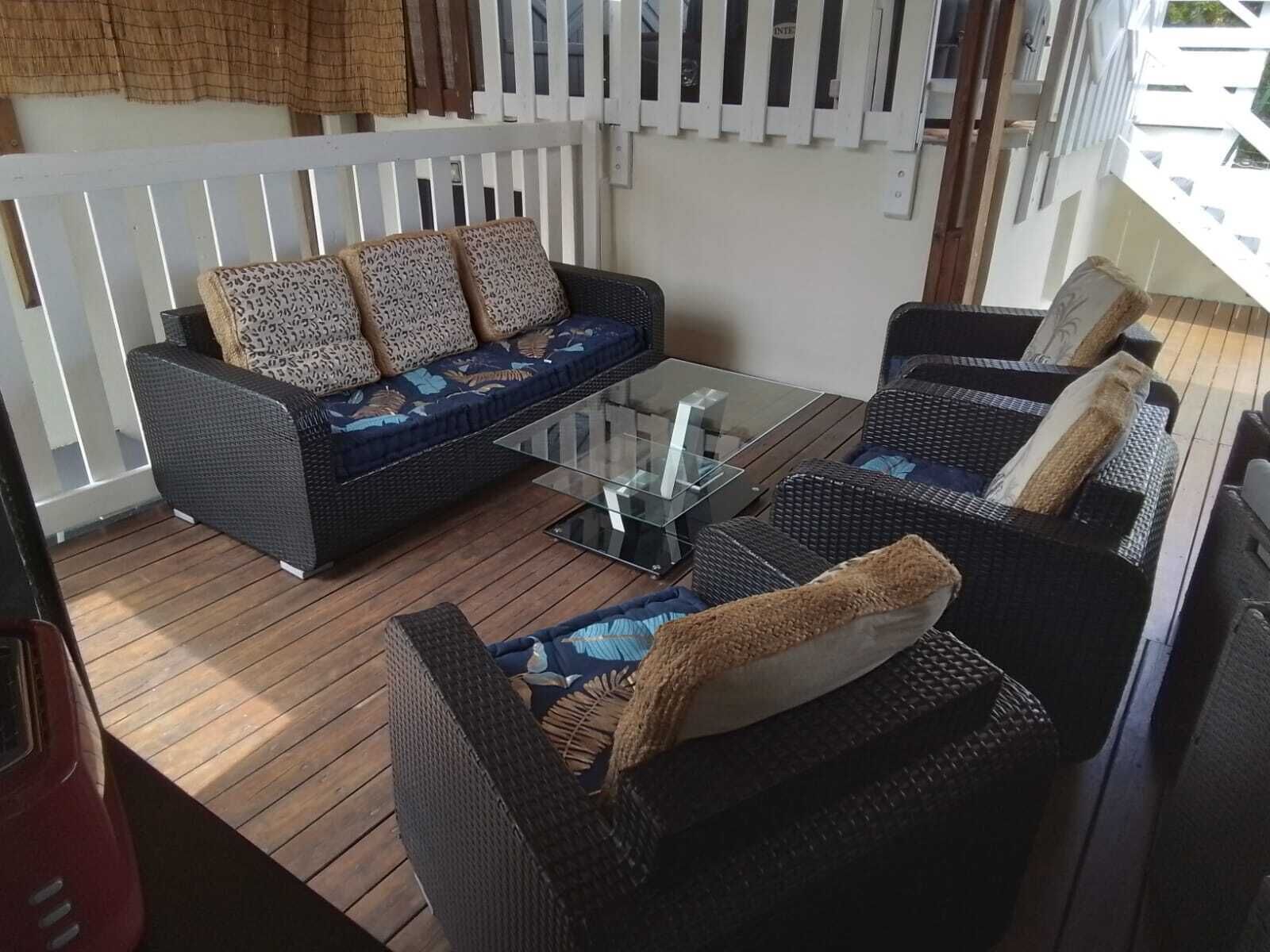 Una terraza con mobiliario de mimbre, que incluye un sofá y dos sillones, junto con una mesa de centro de vidrio.