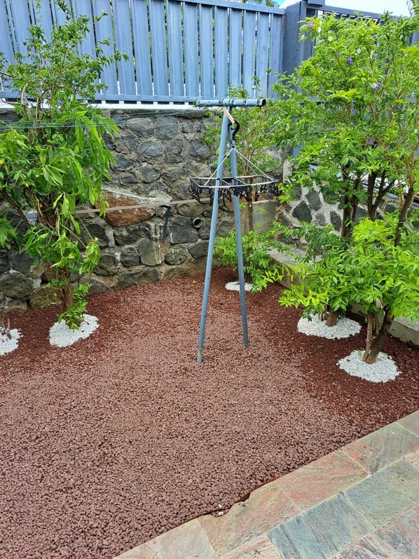 A garden with a stone wall, a swing set, and various plants.