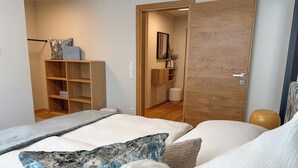 A modern bedroom with a bed, a wardrobe, and a bathroom visible through an open door. - "THREE" - Premium Apartments Seekirchen, modern and central, close to the lake (Seekirchen)