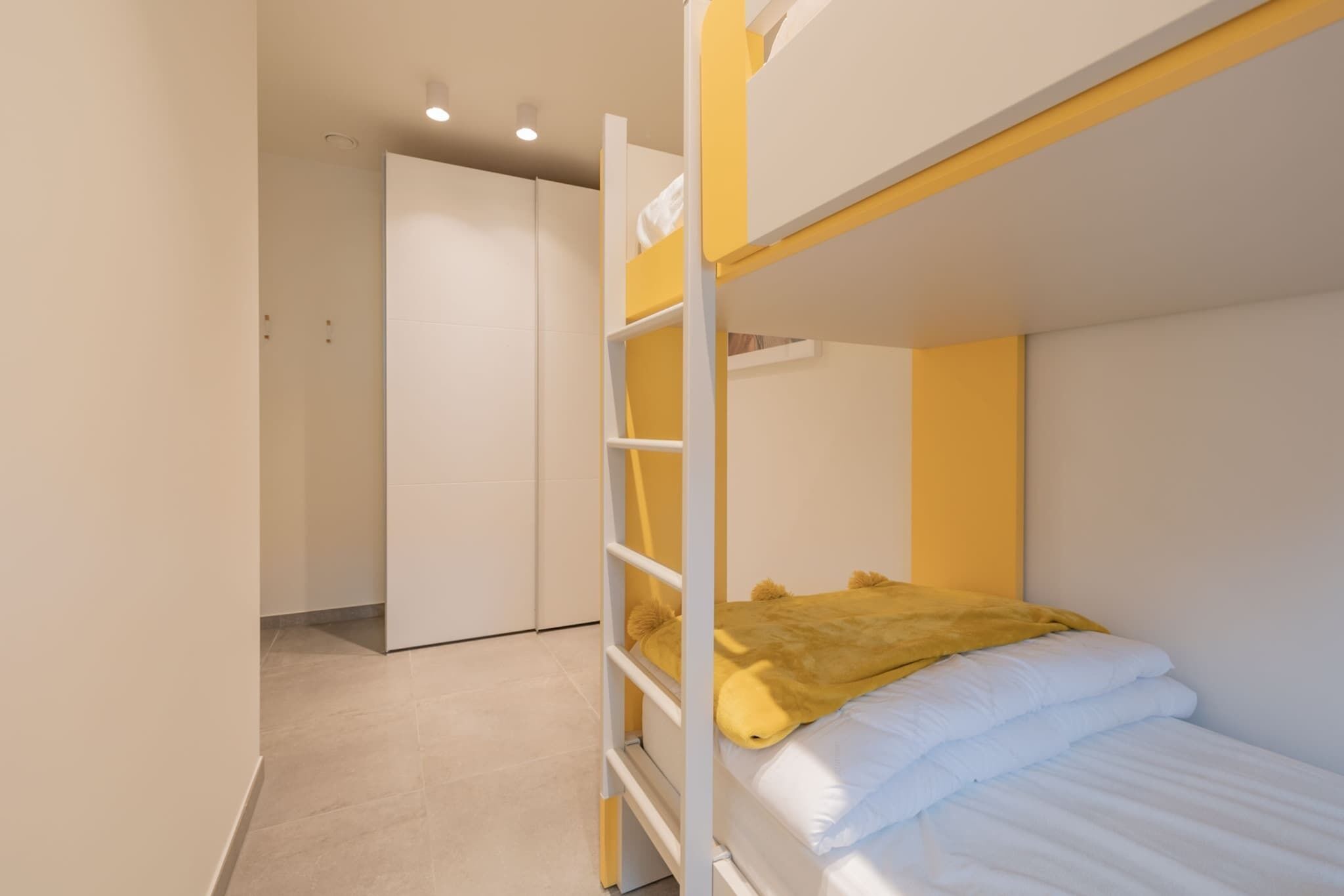 A bunk bed room with a yellow headboard, white bedding, and a closed door in the background.