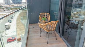 Un balcone con sedie in vimini, un tavolino con una pianta e vista sulla città, inclusa una costruzione particolare e una strada con veicoli.