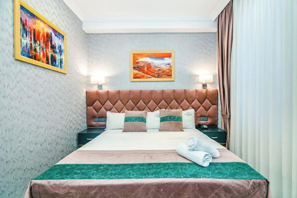 Ein Hotelzimmer mit einem Bett, zwei Nachttischen, einer Kopfteil und zwei Wandlampen.