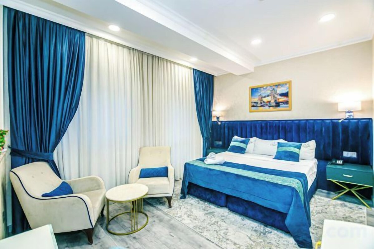 A hotel room with a bed, two armchairs, a small round table, and a nightstand.
