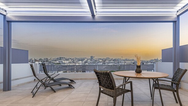Une terrasse sur le toit offrant une vue sur la ville, une table ronde avec des chaises et un vase rempli de fleurs.