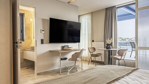 Une chambre d’hôtel moderne dotée d’un grand lit, d’un bureau avec deux chaises, d’une télévision à écran plat et d’une grande fenêtre offrant une vue sur la ville.